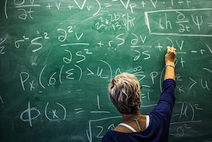 The image features a woman writing math calculations on a large chalkboard.