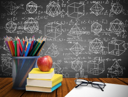 Picture of a desk in front of a chalkboard. The desk has a cup of colored pencils, books, an apple, a piece of paper, and glasses.