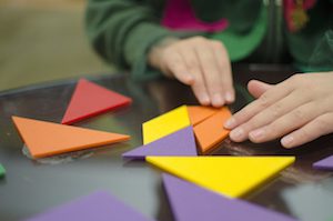 The image features hands arranging math geometric tiles.